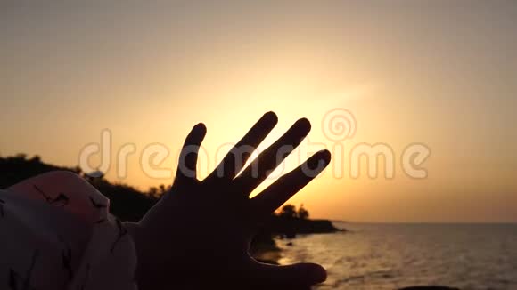 女孩在黎明时分的海上与升起的太阳玩耍处理手指间的太阳射线视频的预览图