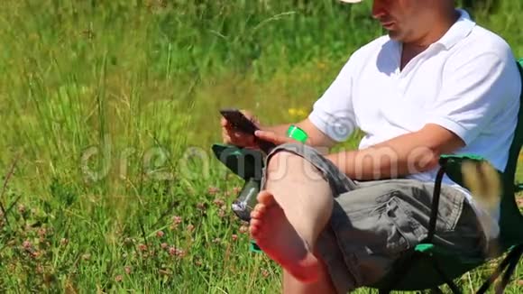 一个男人坐在折叠的野餐椅上在智能手机里玩然后他站起来离开视频的预览图