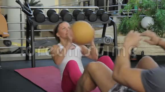 这对夫妇在现代健身房的训练中在粉红色的垫子上做仰卧起坐视频的预览图
