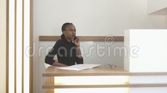 在接待处的年轻非裔美国女孩正在通过手机交谈并在表格中填写一些东西办公室视频的预览图
