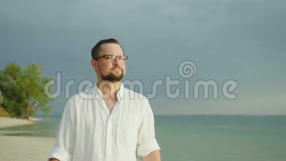 一个穿着宽松衬衫的年轻人沿着海滩散步在热带度假胜地度假视频的预览图