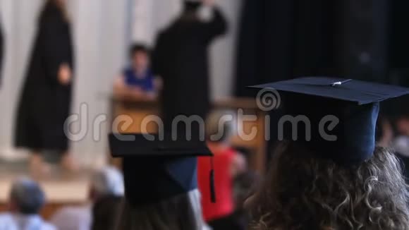 戴着帽子和长袍的快乐学生观看毕业典礼领取毕业证书视频的预览图