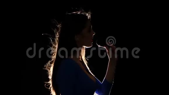 穿着蓝色弗兰克上衣的女孩对着麦克风唱歌黑色背景剪影视频的预览图