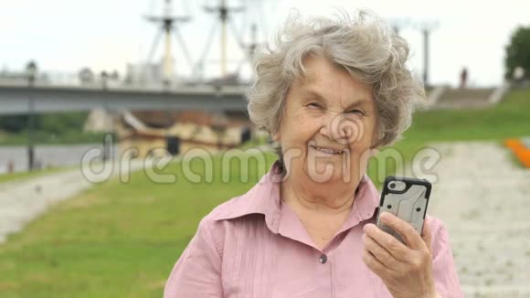 微笑的老年妇女展示银色手机视频的预览图