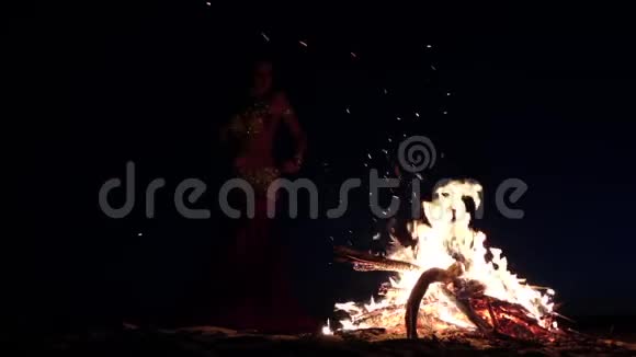 晚上一个女孩在沙滩上跳舞肚皮舞在明亮的篝火旁慢动作剪影视频的预览图