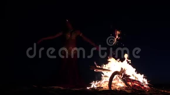 深夜一个女孩在沙滩上跳舞肚皮舞在明亮的篝火旁慢动作剪影视频的预览图