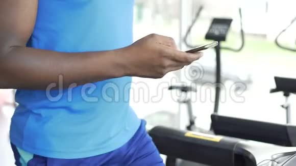 运动员在跑步机上行走并在智能手机上使用健身应用程序视频的预览图