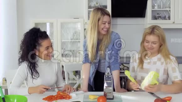 三个年轻的女朋友在家里的厨房准备沙拉然后聊天视频的预览图