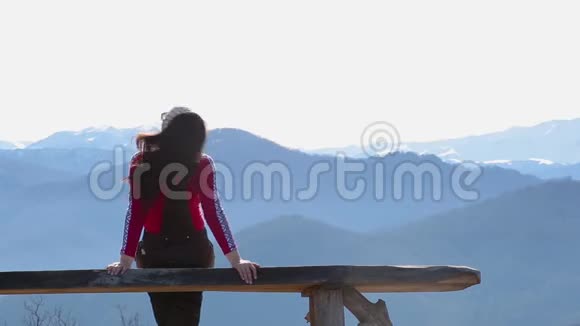年轻女子坐在外面的长凳上看着有山的图画景观视频的预览图