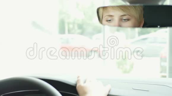 漂亮的金发女郎坐在车里看后视镜微笑着视频的预览图