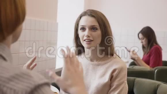 三个白种人年轻女孩坐在咖啡馆里微笑交谈对话惊讶的情绪八卦的概念视频的预览图