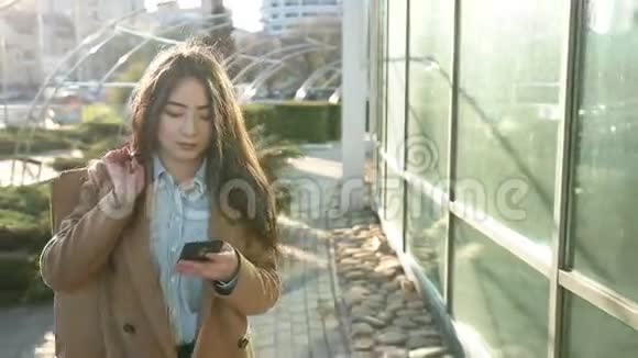 微笑的亚洲女人在户外智能手机上发短信视频的预览图