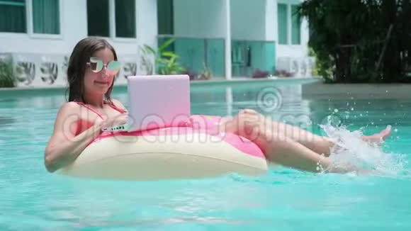 年轻女子在海里游泳在游泳圈里游泳女孩躺在游泳池里用电脑在一个充气的圆圈上顶部视频的预览图