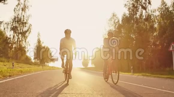 一对骑自行车的夫妇在日落时分骑着自行车走在公路上在高处玩耍视频的预览图