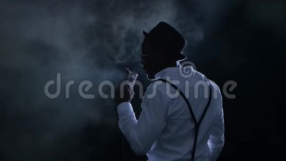 歌手从后面的烟雾和白光唱成复古麦克风并在它附近跳舞黑色视频的预览图