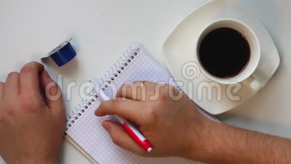 男人在咖啡里吃奶油然后他拿起一支笔思考在笔记本上写什么他不时地喝咖啡视频的预览图