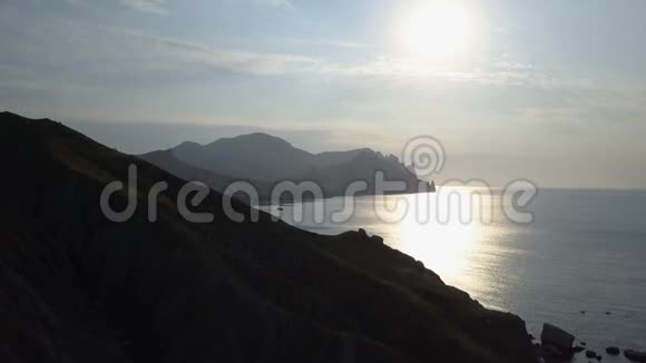 日出时飞越海洋和山脉克里米亚卡拉达格山的鸟瞰图视频的预览图