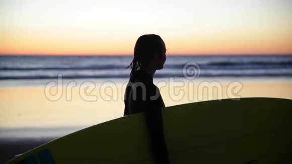 小女孩拿着冲浪板在海滩上女人在海岸边冲浪女人的剪影美丽美丽视频的预览图
