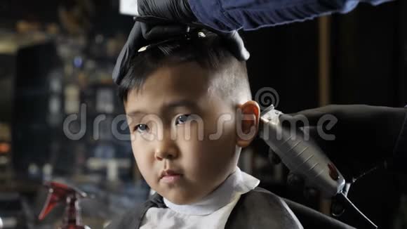 戴着黑色手套的理发师轻轻地剃掉一个亚洲小孩耳朵后面的头发60英尺视频的预览图