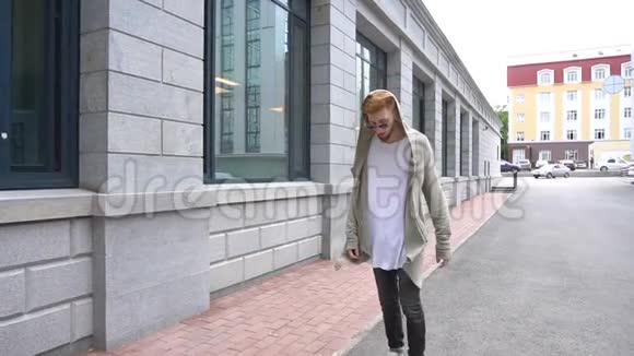 一个穿着时髦衣服的年轻红头发男人的照片正在现代小镇上走来走去视频的预览图