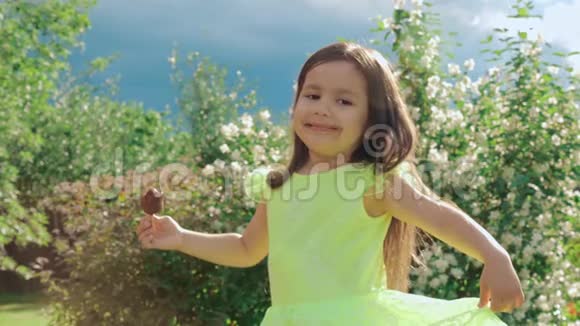 一个穿着亮绿色连衣裙的小可爱和有趣的女孩做鬼脸吃冰淇淋视频的预览图