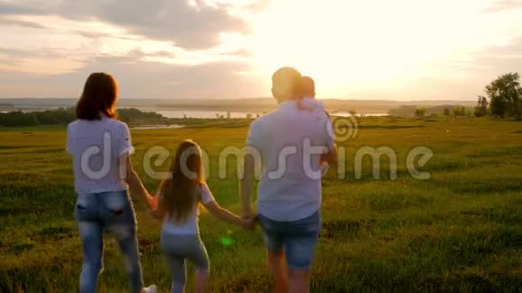 快乐的年轻家庭有两个孩子在夏天的田野上奔跑健康的母亲父亲和儿童享受大自然视频的预览图