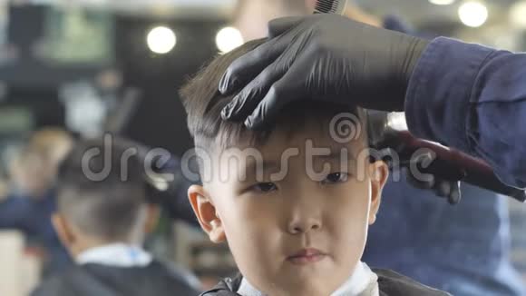 戴着黑手套的理发师在理发店里仔细地剃掉一个亚洲孩子的威士忌前景60英里视频的预览图