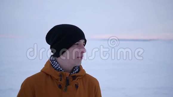 冬天一个穿着橙色夹克和帽子的英俊的年轻人微笑视频的预览图