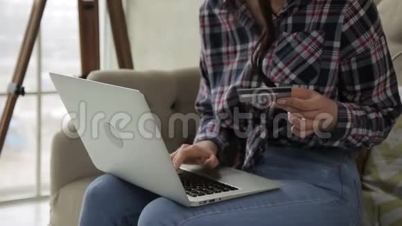 年轻女子带着笔记本电脑和信用卡坐在公寓里视频的预览图