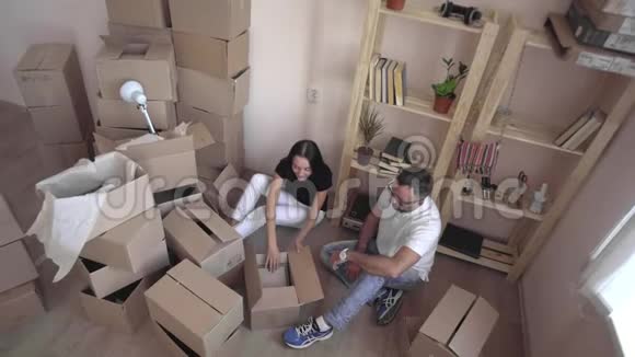把一个年轻的家庭搬到一个新的公寓丈夫和妻子互相拥抱坐在地板上周围是盒子和视频的预览图
