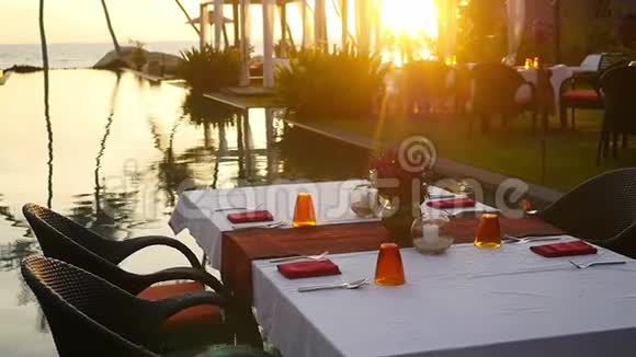 在热带岛屿的餐桌前棕榈树和游泳池在惊人的日落慢动作1920x1080视频的预览图