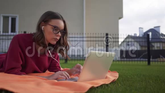 一个穿着笔记本电脑躺在草地上的女孩视频的预览图