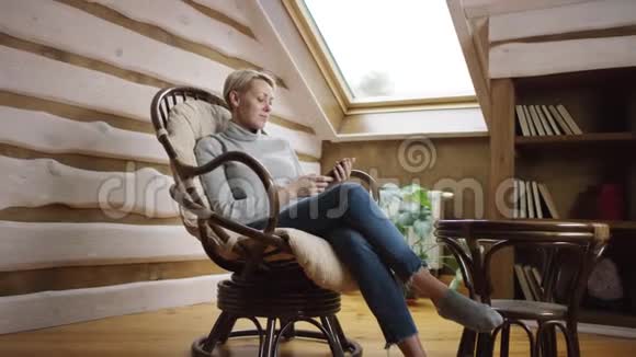金发女人坐在椅子上用智能手机上网视频的预览图