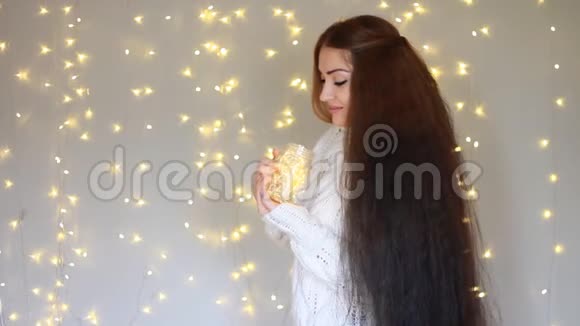美丽的女人穿着温暖的白色毛衣手里拿着一盏灯闭上眼睛在灯光的背景下做梦视频的预览图