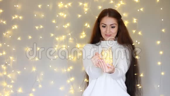 穿着白色毛衣的漂亮女人手里拿着一盏灯闭上眼睛在灯光的背景下做梦视频的预览图