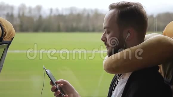 长胡子的人坐公共汽车拿着智能手机听着耳机上的音乐视频的预览图