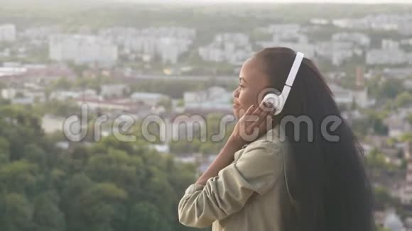 迷人的非裔美国女孩听音乐感到快乐微笑着年轻的黑人女孩模糊的城市背景视频的预览图