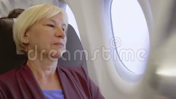 坐飞机的高级女人在湍流中女性在靠近窗户时感到疲倦视频的预览图