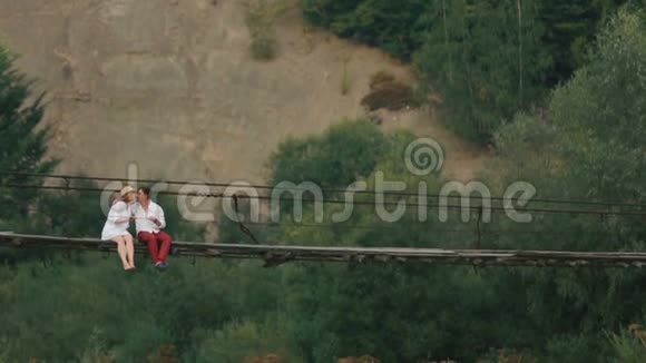 在河对岸的一座挂着的木桥上有一对快乐的恋人在亲吻着无人机视频的预览图