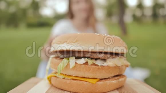 一个学生女孩用手拿一个煮熟的汉堡包她在露天吃夏天娱乐视频的预览图