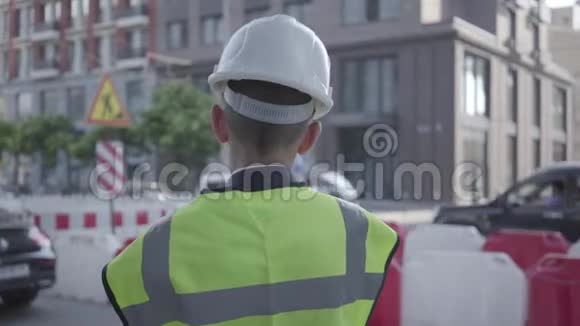 一个小男孩穿着商务服安全装备和建筑工人头盔站在大城市的繁忙道路上视频的预览图
