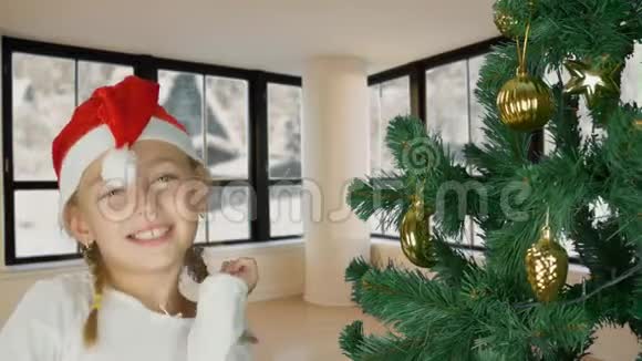 圣诞老人戴着红帽子在圣诞树旁跳舞的快乐少女快乐的年轻白种人女孩圣诞树客厅视频的预览图