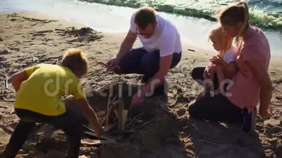 一个带着孩子的小家庭正在海滩野餐的海边生火视频的预览图