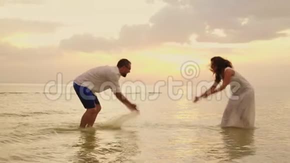 年轻夫妇在海里玩得很开心互相泼水日落时分慢速视频视频的预览图