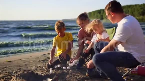 在一个风和日丽的夏日一家人把棉花糖放在海边的烤串上视频的预览图