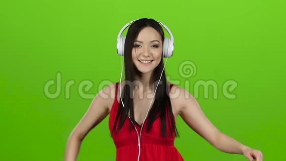 女孩通过耳机和舞蹈听欢快的音乐绿色屏幕慢动作视频的预览图