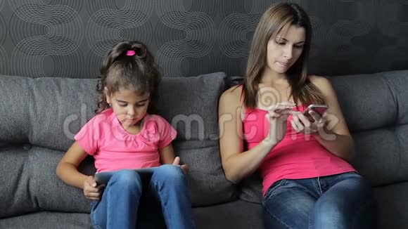 现代家庭价值观电子奴役有孩子的妈妈坐在沙发上用平板电脑和智能手机视频的预览图