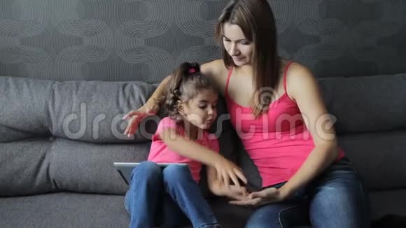 母亲带着孩子坐在沙发上用平板电脑女人会让坐在沙发上的婴儿痒痒在训练中吐口水视频的预览图