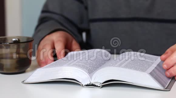 一个年轻人坐在桌子旁拿着一块银片读圣经然后他合上了书视频的预览图