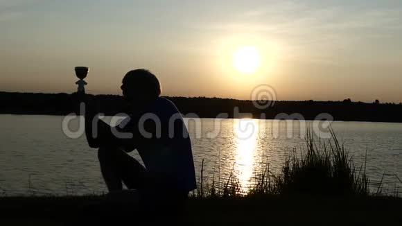 快乐的人坐着看着他的冠军碗在一个湖岸的斯洛文尼亚视频的预览图